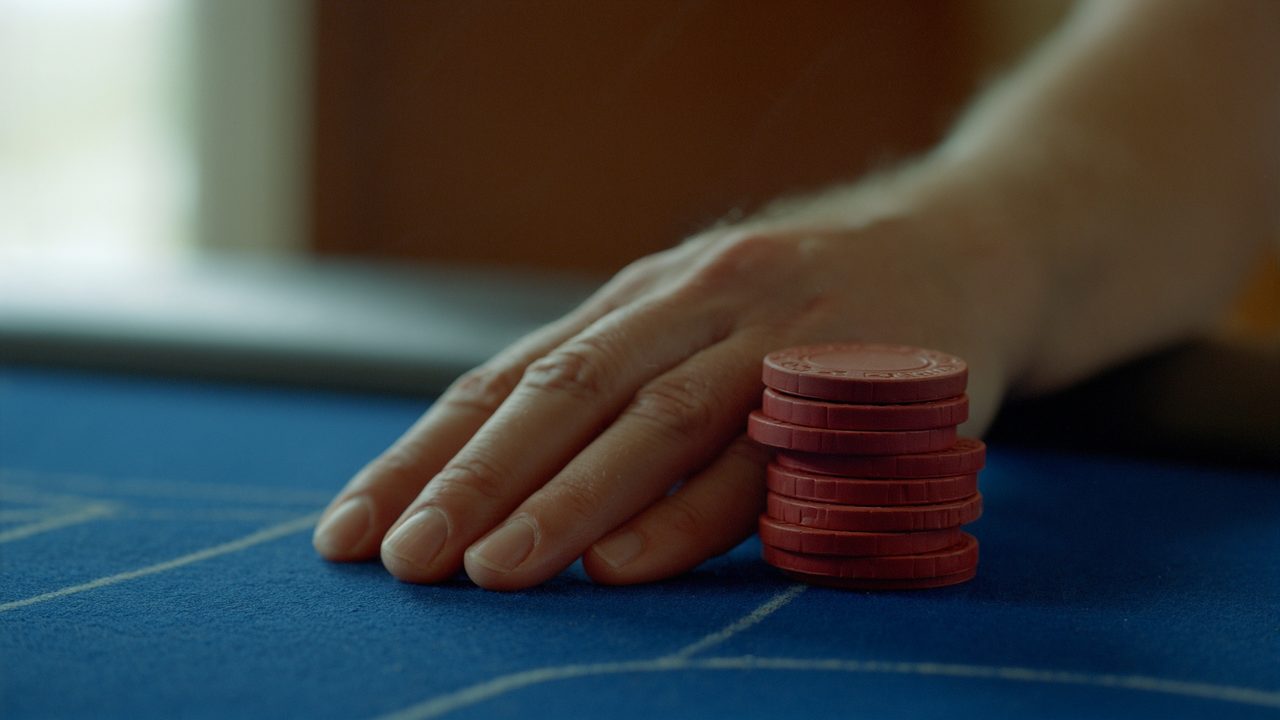 A hand resting on blue casino felt beside a short stack of red clay chips